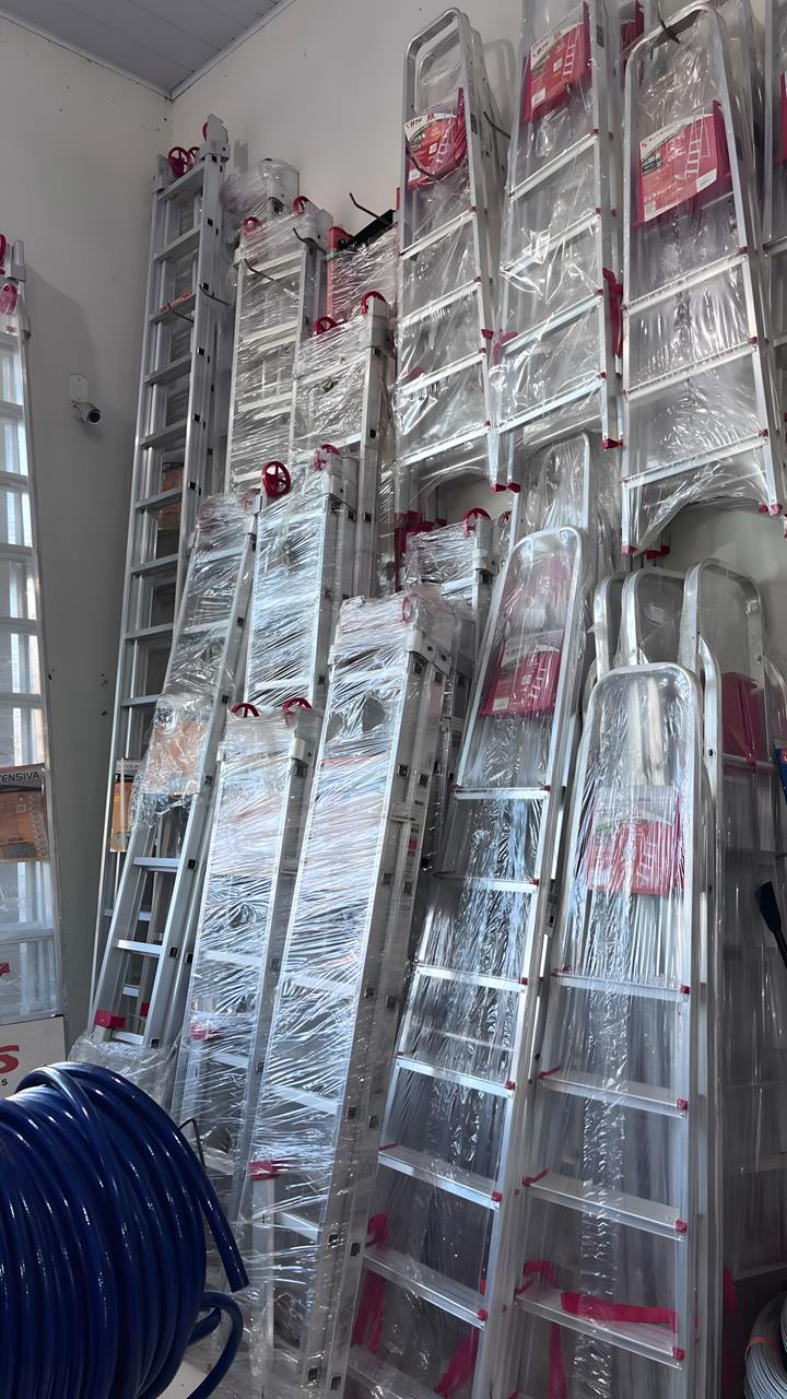 Escadas de alumínio de abrir e extensíveis, de vários tamanhos, encostadas na parede da loja