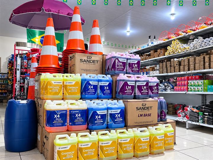 Galões de produtos de lavagem automotiva empilhados, cones de sinalização e prateleiras cheias na loja